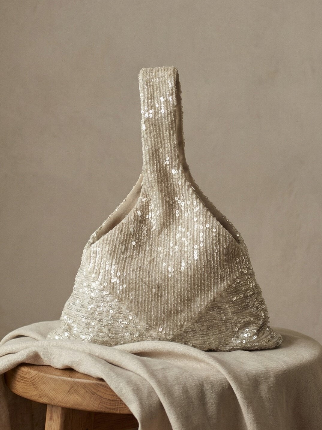 Champagne sequin bridal clutch displayed on a draped fabric surface