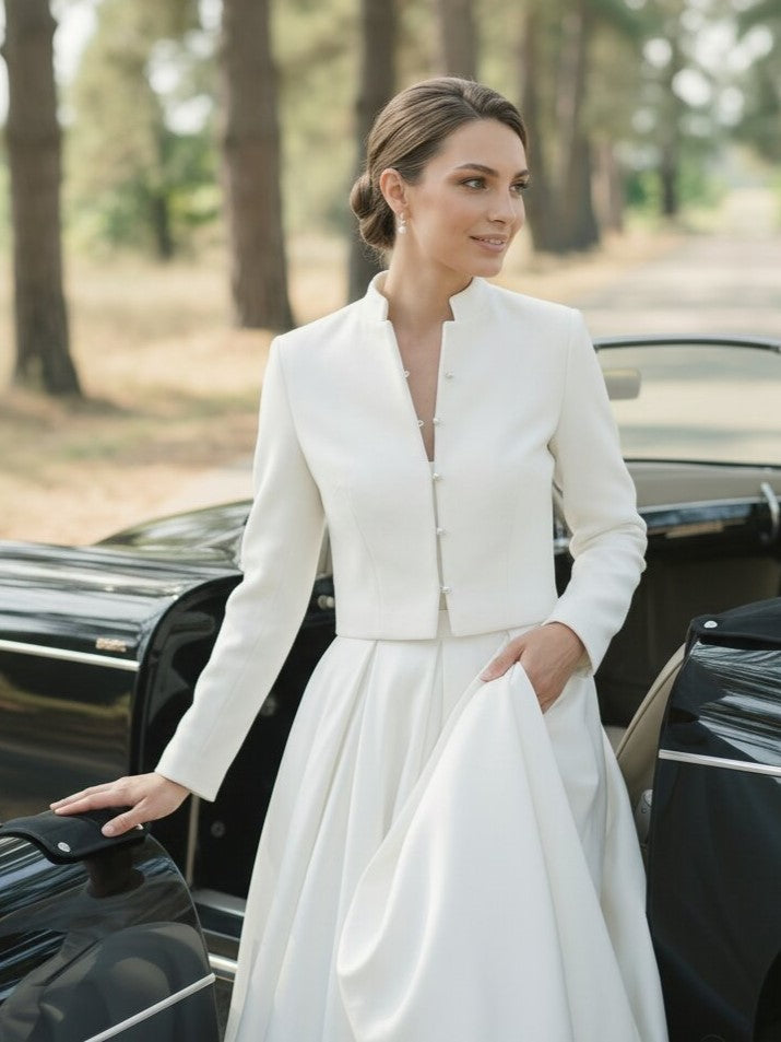 Woman in a white bridal outfit standing next to a vintage car in a forest setting