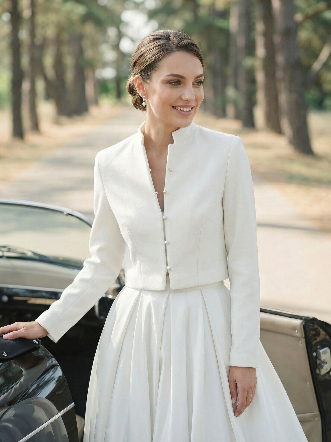 Bride wearing a cropped ivory bridal jacket with pearl buttons over a flowing white wedding dress