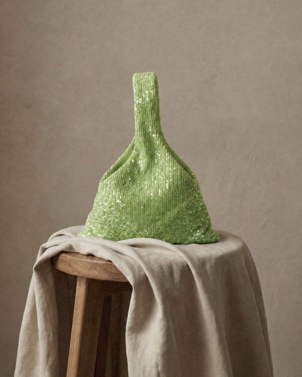 Sage green sequin bridal clutch displayed on a draped fabric surface