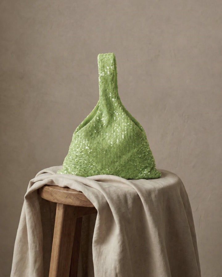 Sage green sequin bridal clutch displayed on a draped fabric surface