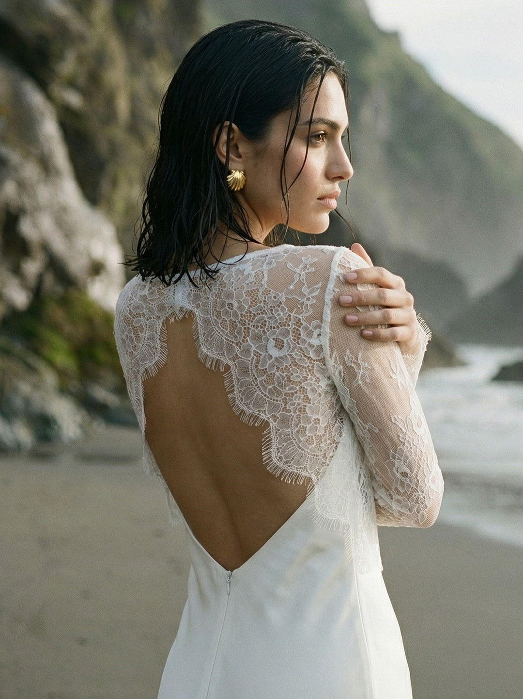 Bride showing the sheer lace back of a white wedding dress blouse on the beach