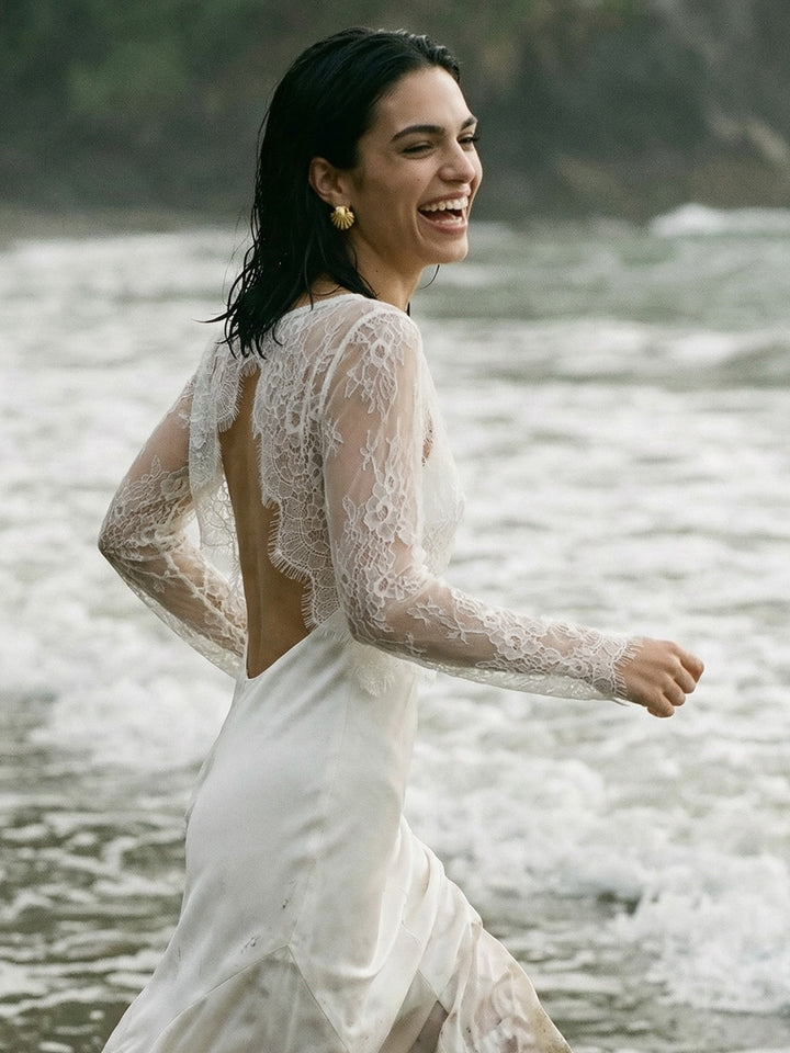 Bride in a sheer lace blouse walking along the beach in a white wedding dress