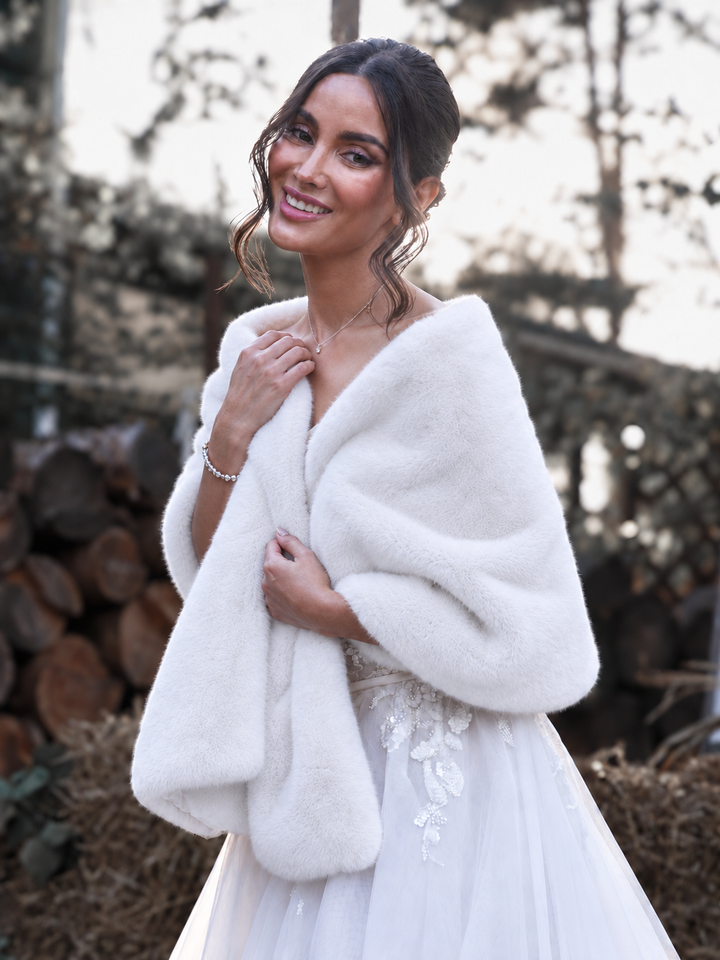 Bride wearing a soft white faux fur shawl over a wedding dress outdoors